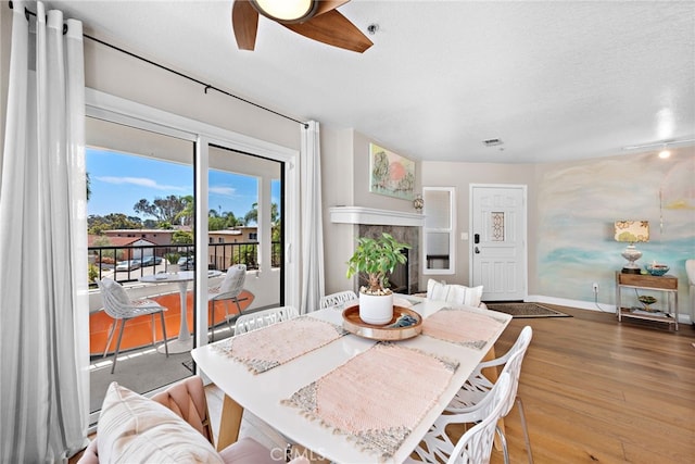 dining space with a textured ceiling, ceiling fan, a tiled fireplace, and hardwood / wood-style floors