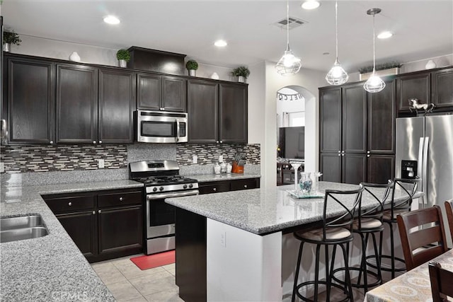 1714 Graybark Ave, Clovis, CA 93619 - kitchen featuring arched walkways, a breakfast bar, light stone counters, stainless steel appliances, and decorative backsplash