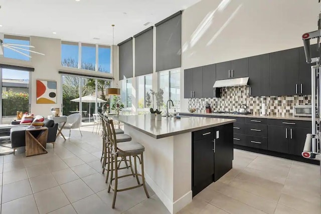 kitchen featuring a breakfast bar, decorative backsplash, a towering ceiling, a kitchen island with sink, and appliances with stainless steel finishes