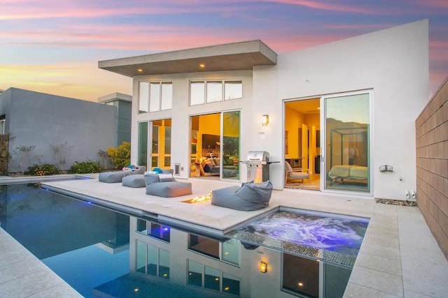 back house at dusk with an in ground hot tub and a patio area