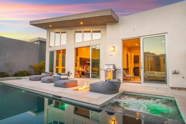 back house at dusk with a pool with hot tub, a patio area, and a fire pit