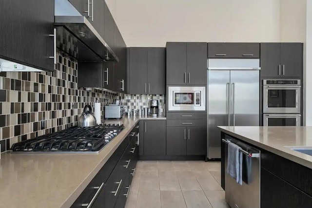 kitchen with light tile patterned flooring, extractor fan, built in appliances, and tasteful backsplash