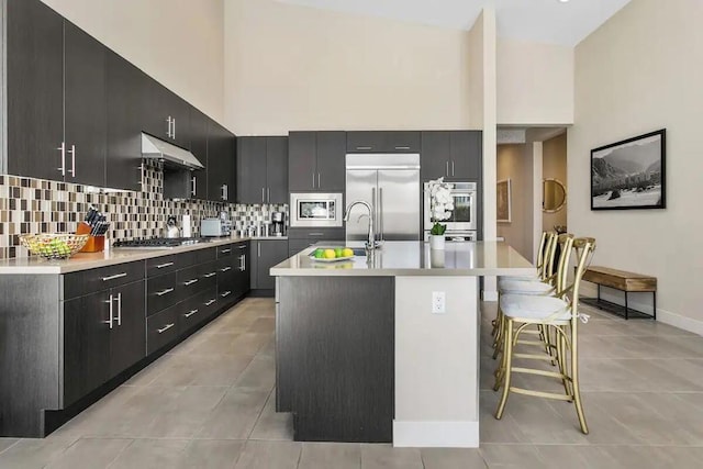 kitchen featuring a kitchen bar, sink, a high ceiling, built in appliances, and a kitchen island with sink