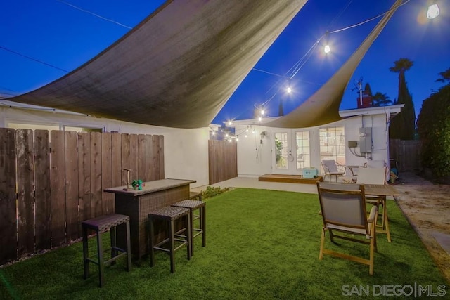 back house at twilight with a patio area, a yard, and french doors