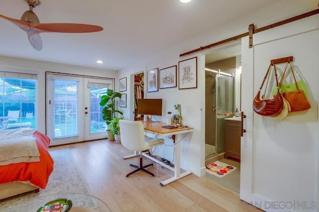 bedroom with light hardwood / wood-style floors, a barn door, ceiling fan, access to outside, and ensuite bath