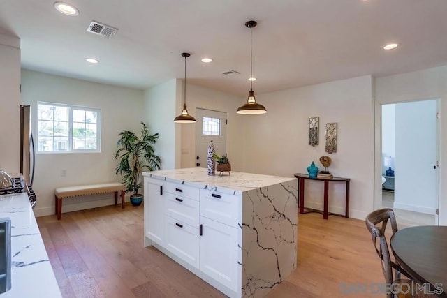 kitchen with a kitchen island, white cabinetry, hanging light fixtures, light wood-type flooring, and light stone countertops