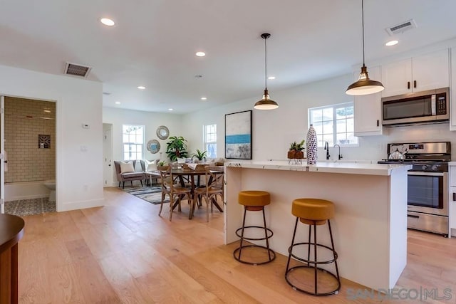 kitchen with an island with sink, appliances with stainless steel finishes, decorative light fixtures, a wealth of natural light, and white cabinets