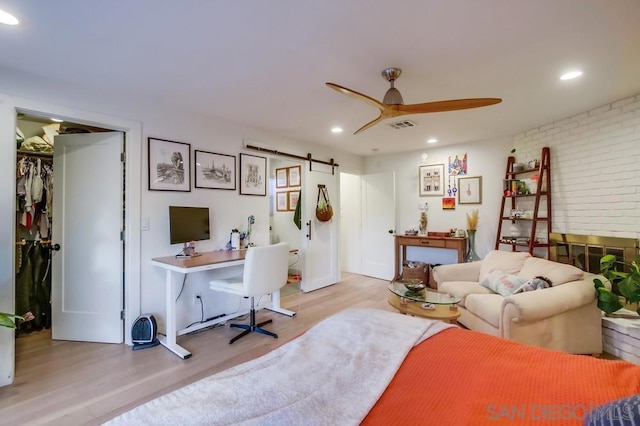 office space featuring ceiling fan, brick wall, light hardwood / wood-style floors, and a barn door