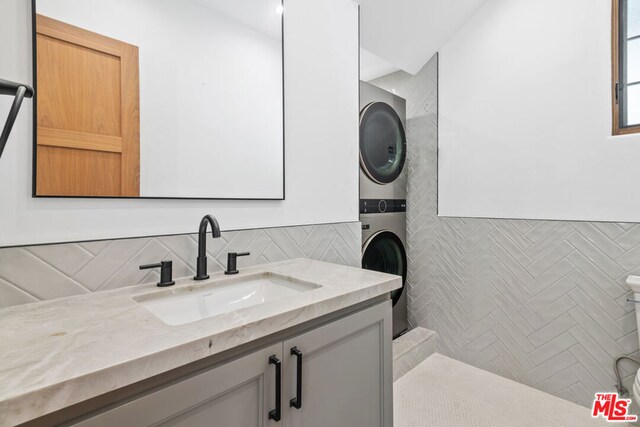 bathroom featuring decorative backsplash, stacked washer / dryer, and vanity