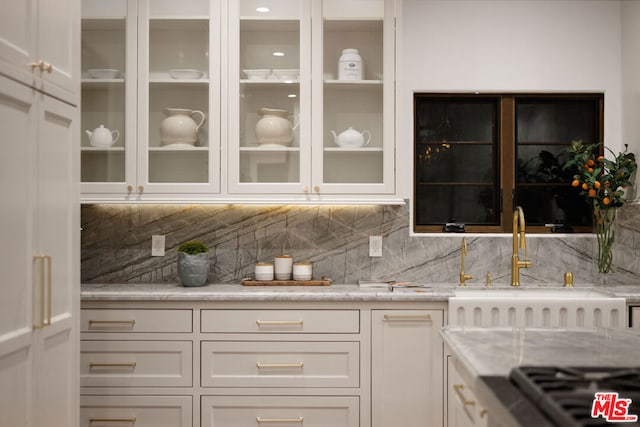 bar featuring white cabinets, decorative backsplash, light stone countertops, and sink