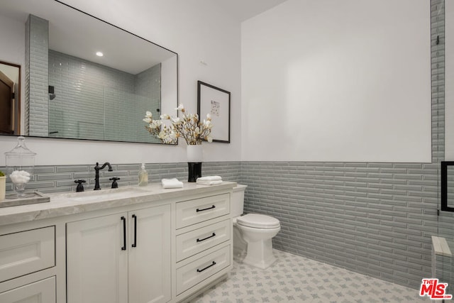 bathroom with tile patterned floors, a shower with door, vanity, tile walls, and toilet