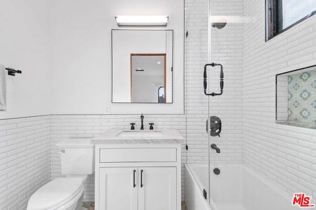 full bathroom featuring combined bath / shower with glass door, vanity, tile walls, and toilet