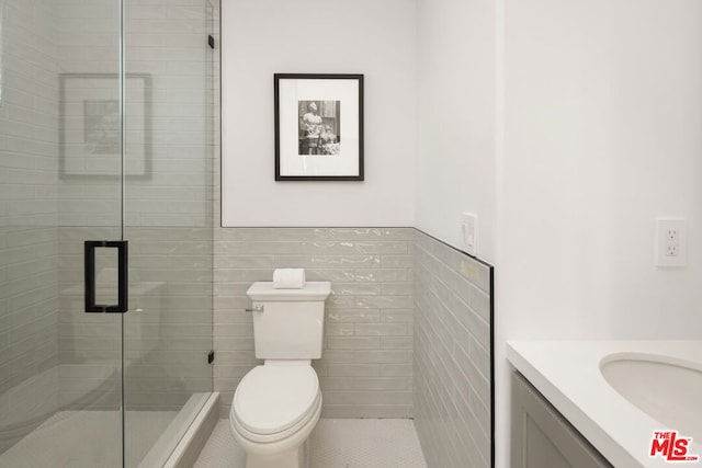 bathroom with toilet, a shower with door, tile patterned flooring, tile walls, and vanity