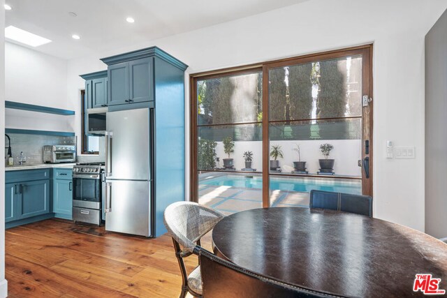 kitchen featuring a skylight, appliances with stainless steel finishes, blue cabinets, and dark hardwood / wood-style floors