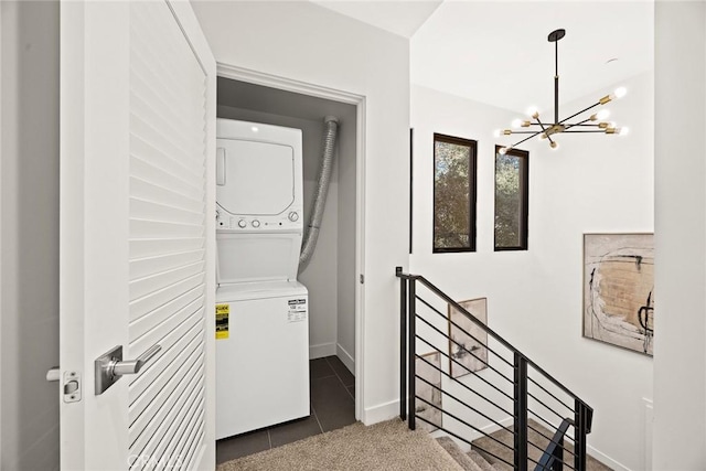 laundry room with dark tile patterned floors, stacked washer and dryer, and an inviting chandelier