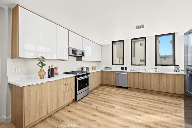 kitchen with appliances with stainless steel finishes, sink, white cabinetry, and light hardwood / wood-style flooring