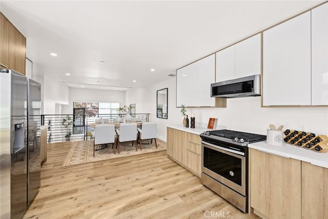 kitchen featuring appliances with stainless steel finishes, light hardwood / wood-style flooring, and white cabinetry