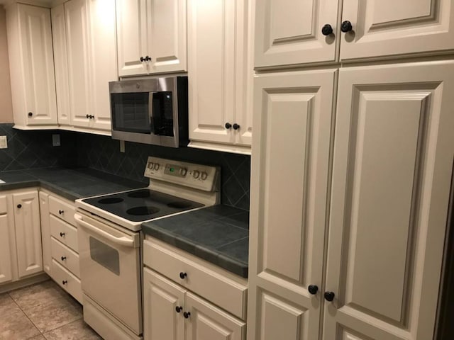 kitchen featuring white cabinets, electric range, light tile patterned flooring, and tasteful backsplash