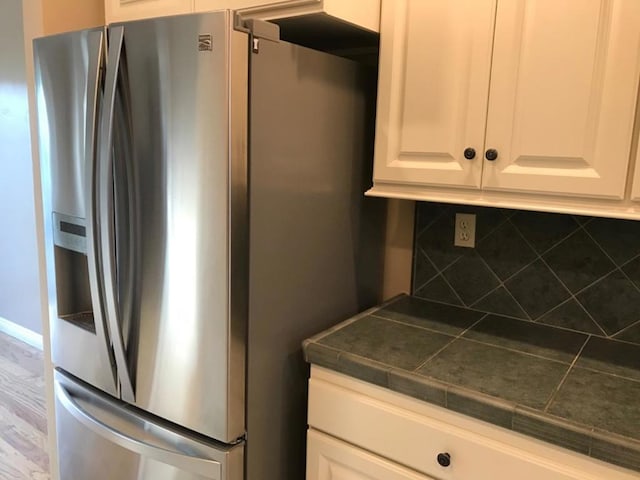 kitchen featuring hardwood / wood-style floors, stainless steel fridge, tasteful backsplash, and white cabinetry