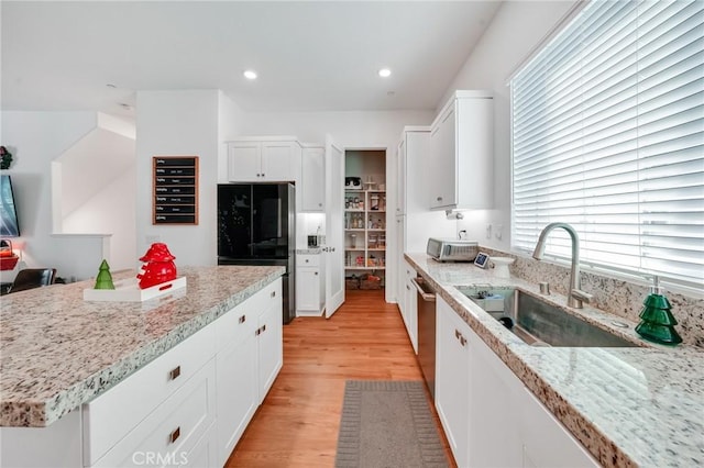 kitchen with light stone counters, sink, white cabinets, and black fridge