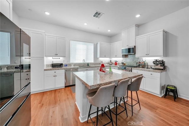 kitchen featuring light hardwood / wood-style floors, a kitchen island, appliances with stainless steel finishes, a kitchen breakfast bar, and white cabinets