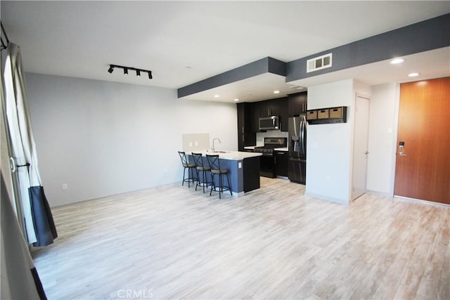 kitchen featuring appliances with stainless steel finishes, light hardwood / wood-style flooring, sink, a breakfast bar, and a center island with sink