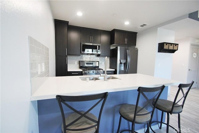 kitchen with light hardwood / wood-style floors, a breakfast bar area, stainless steel appliances, decorative backsplash, and sink