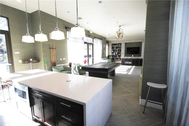 kitchen featuring dark parquet flooring, a kitchen island, hanging light fixtures, billiards, and a notable chandelier