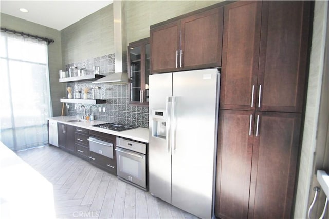 kitchen with wall chimney range hood, decorative backsplash, appliances with stainless steel finishes, and sink