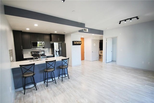 kitchen with appliances with stainless steel finishes, a kitchen bar, tasteful backsplash, sink, and light hardwood / wood-style flooring