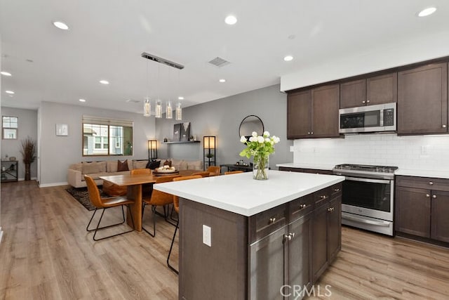 kitchen with hanging light fixtures, light wood-type flooring, stainless steel appliances, and a kitchen island