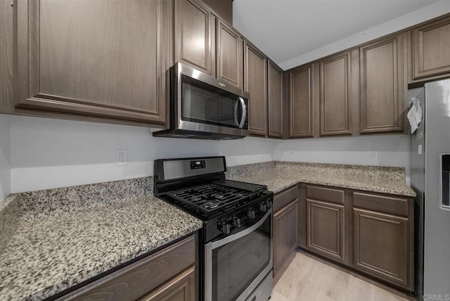 kitchen featuring light hardwood / wood-style floors, light stone countertops, dark brown cabinetry, and appliances with stainless steel finishes