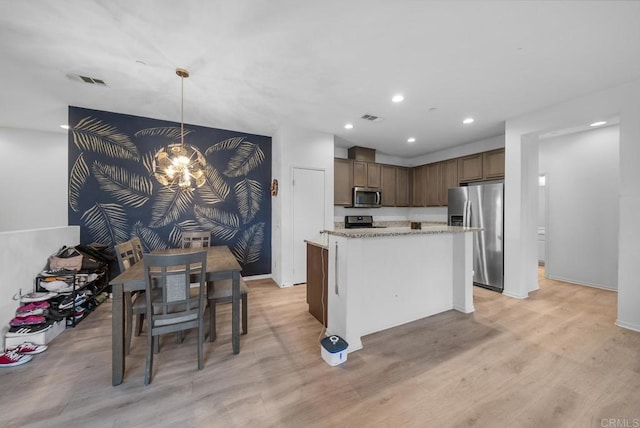 kitchen featuring stainless steel appliances, light wood-type flooring, hanging light fixtures, light stone counters, and a center island