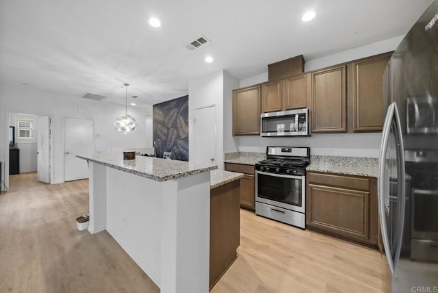 kitchen featuring stainless steel appliances, pendant lighting, light hardwood / wood-style flooring, light stone counters, and a center island