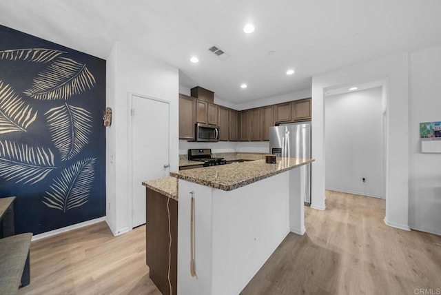 kitchen featuring a center island, light hardwood / wood-style flooring, dark brown cabinetry, stainless steel appliances, and light stone counters