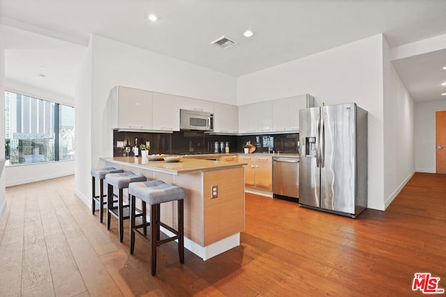 kitchen with white cabinets, appliances with stainless steel finishes, decorative backsplash, light wood-type flooring, and a breakfast bar area