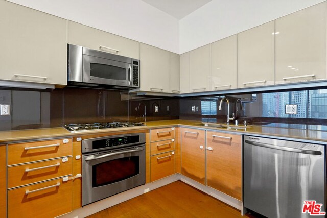 kitchen with tasteful backsplash, stainless steel counters, light hardwood / wood-style floors, sink, and appliances with stainless steel finishes