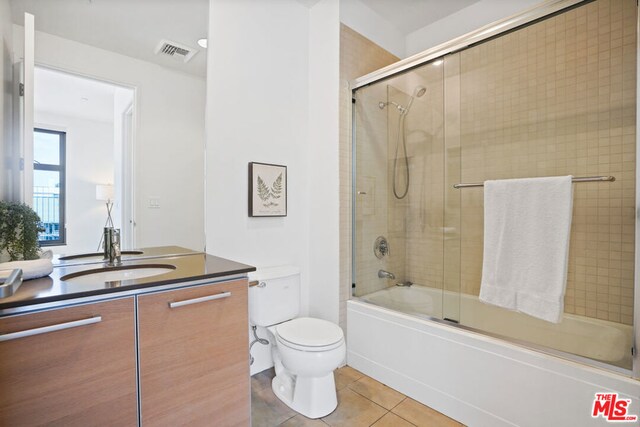 full bathroom with combined bath / shower with glass door, vanity, tile patterned floors, and toilet