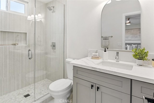 bathroom featuring a shower with shower door, toilet, vanity, and ceiling fan