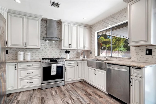 kitchen featuring sink, white cabinetry, light hardwood / wood-style flooring, stainless steel appliances, and wall chimney exhaust hood