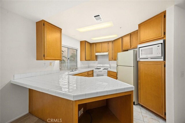 kitchen featuring kitchen peninsula, sink, white appliances, light tile patterned flooring, and tile counters