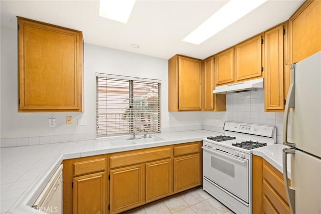 kitchen with a skylight, tile countertops, white appliances, light tile patterned flooring, and sink