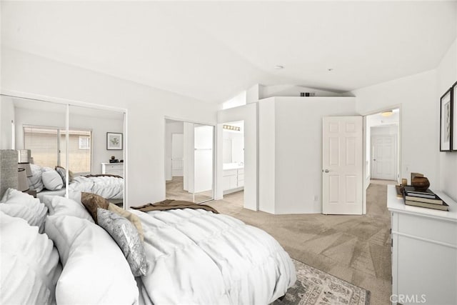 bedroom featuring ensuite bathroom, light colored carpet, and vaulted ceiling