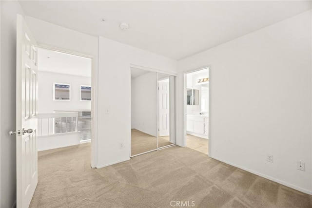 unfurnished bedroom with ensuite bathroom, light colored carpet, and a closet