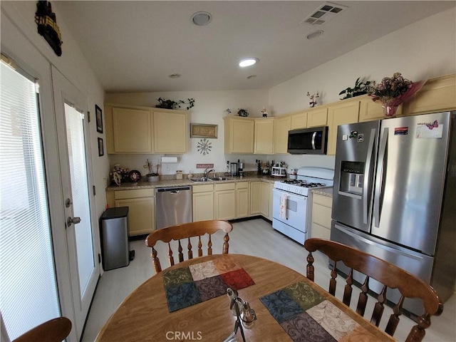 kitchen featuring light stone countertops, vaulted ceiling, appliances with stainless steel finishes, cream cabinetry, and sink