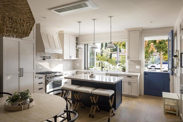 kitchen with tasteful backsplash, a center island, custom exhaust hood, high end stainless steel range, and white cabinets