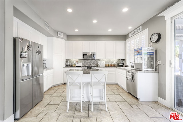 kitchen featuring white cabinets, appliances with stainless steel finishes, a kitchen island, a kitchen bar, and sink