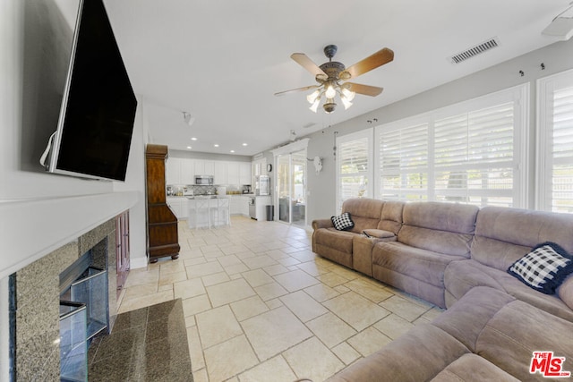 tiled living room with ceiling fan and a fireplace