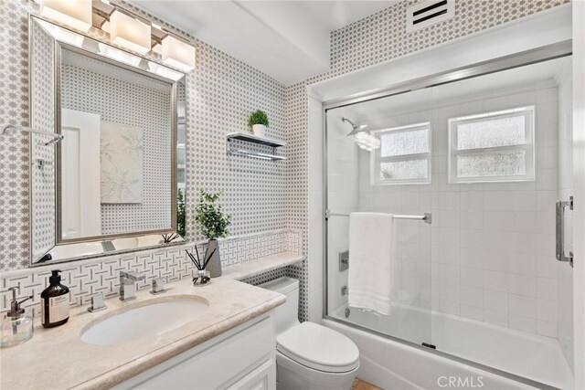 full bathroom featuring toilet, tasteful backsplash, vanity, and shower / bath combination with glass door