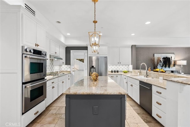 kitchen featuring appliances with stainless steel finishes, light stone counters, hanging light fixtures, and a center island